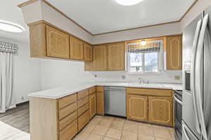 Kitchen featuring stainless steel appliances, light countertops, crown molding, light tile patterned floors, and a peninsula