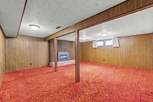 Below grade area featuring a fireplace, wooden walls, carpet flooring, and a textured ceiling