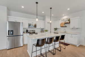 Kitchen featuring stainless steel appliances, decorative light fixtures, a breakfast bar, white cabinetry, and a kitchen island
