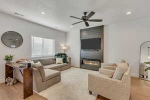 Living area with light wood finished floors, a ceiling fan, a fireplace, and recessed lighting