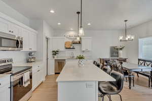 Kitchen featuring stainless steel appliances, a breakfast bar area, a kitchen island, light wood finished floors, and white cabinetry