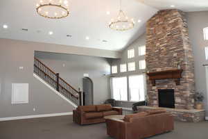 Living room featuring arched walkways, a chandelier, a stone fireplace, carpet, and vaulted ceiling