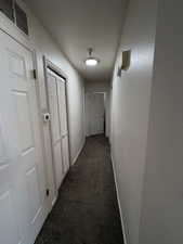 Hall featuring dark colored carpet and baseboards