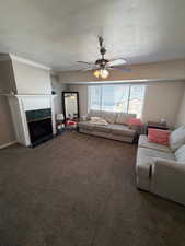 Carpeted living room featuring a ceiling fan, a textured ceiling, ornamental molding, and a fireplace with flush hearth