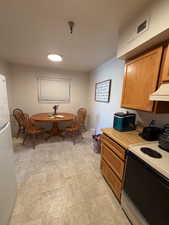Kitchen with electric range, light countertops, freestanding refrigerator, extractor fan, and wood finish cabinets