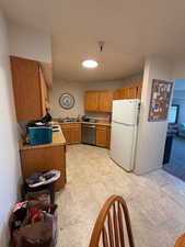 Kitchen featuring light countertops, freestanding refrigerator, wood finish cabinets, stainless steel dishwasher, and stone finish floors
