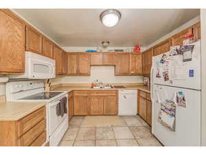 Kitchen featuring white appliances, light countertops, wood finish cabinets, and light tile patterned floors