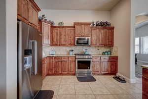 Kitchen with stainless steel appliances, wood finish cabinetry, light tile patterned floors, and light stone countertops