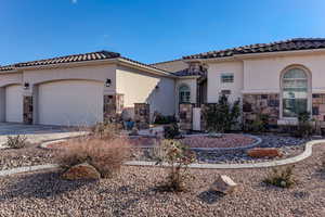 Mediterranean / spanish-style house with stone siding, stucco siding, an attached garage, and concrete driveway