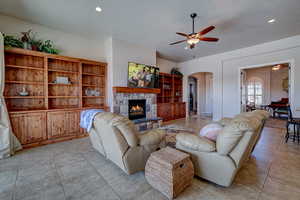 Living area featuring arched walkways, a stone fireplace, ceiling fan, light tile patterned flooring, and recessed lighting