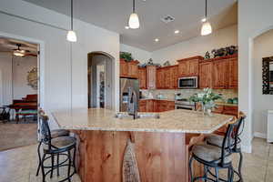 Kitchen featuring arched walkways, light tile patterned floors, a kitchen breakfast bar, and wood finish cabinets