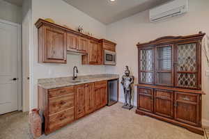 Kitchen featuring light colored carpet, light stone countertops, wood finish cabinetry, and stainless steel microwave