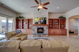 Living area featuring a ceiling fan, arched walkways, a stone fireplace, recessed lighting, and light tile patterned flooring