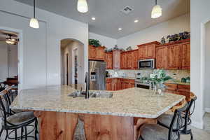 Kitchen featuring a breakfast bar, arched walkways, wood finish cabinetry, hanging light fixtures, and stainless steel appliances