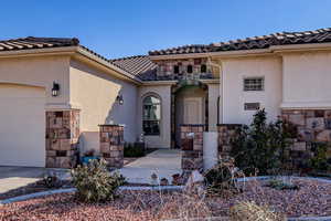 View of exterior entry with stone siding, stucco siding, an attached garage, and driveway