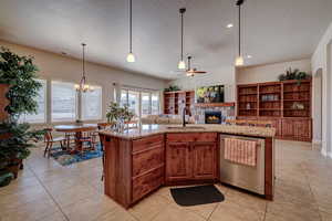 Kitchen with dishwasher, a stone fireplace, light stone counters, a center island with sink, and a textured ceiling