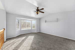 Carpeted empty room with a ceiling fan and vaulted ceiling