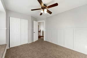 Unfurnished bedroom featuring a decorative wall, wainscoting, carpet flooring, a ceiling fan, and a closet