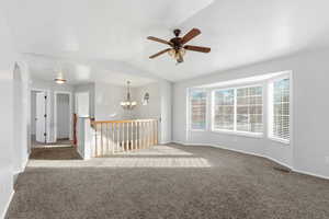 Carpeted empty room featuring ceiling fan, a chandelier, and vaulted ceiling