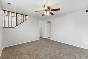 Carpeted spare room featuring ceiling fan and stairway