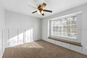 Carpeted spare room with a decorative wall, a wainscoted wall, and a ceiling fan