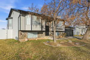Back of house with a yard, stone siding, a garage, and a gate
