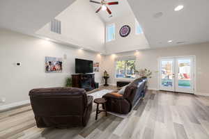 Living room with french doors, a high ceiling, ceiling fan, a glass covered fireplace, and light wood finished floors