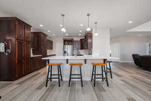 Kitchen with dark wood finish cabinets, open floor plan, a kitchen bar, a peninsula, and stainless steel fridge