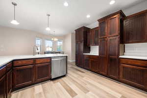 Kitchen with dishwasher, light wood finished floors, dark wood finish cabinets, and suspended lighting