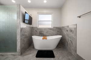 Full bath with tile walls, a freestanding tub, a stall shower, and wainscoting