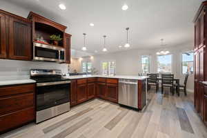 Kitchen with stainless steel appliances, a peninsula, light wood-style flooring, open shelves, and dark wood finish cabinets