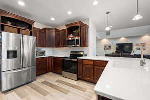 Kitchen with open shelves, stainless steel appliances, open floor plan, hanging light fixtures, and light wood-type flooring