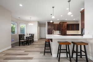 Kitchen featuring a peninsula, a kitchen breakfast bar, light wood-style flooring, a chandelier, and dark wood finish cabinetry