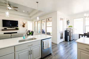 Kitchen featuring a ceiling fan, light countertops, open floor plan, dishwasher, and a raised ceiling