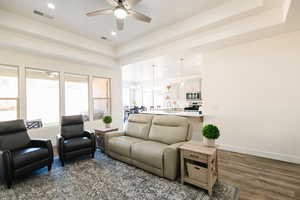 Living area with a tray ceiling, ceiling fan, dark wood-style flooring, and a chandelier