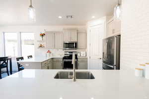 Kitchen featuring stainless steel appliances, pendant lighting, a peninsula, gray cabinetry, and decorative backsplash