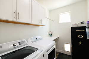Laundry room with washing machine and clothes dryer, dark wood-style floors, and cabinet space