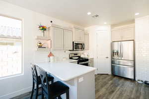 Kitchen featuring stainless steel appliances, dark wood-style floors, light countertops, a peninsula, and a breakfast bar area