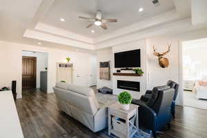 Living area with ceiling fan, recessed lighting, a fireplace, a tray ceiling, and dark wood-style flooring