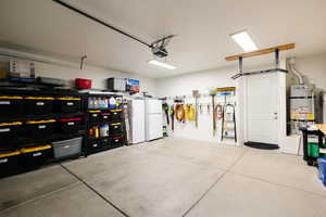 Garage featuring strapped water heater, freestanding refrigerator, and white refrigerator
