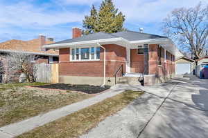 View of front facade featuring an outbuilding, a garage, brick siding, driveway, and a chimney