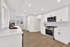 Kitchen with tasteful backsplash, stainless steel appliances, white cabinets, light stone countertops, and light wood-style floors