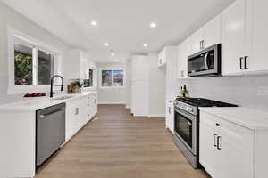 Kitchen featuring tasteful backsplash, stainless steel appliances, white cabinets, light stone countertops, and light wood-style flooring