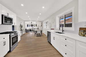Kitchen with tasteful backsplash, white cabinets, stainless steel appliances, light stone countertops, and recessed lighting