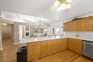 Kitchen featuring hanging lights, light wood finished floors, stainless steel dishwasher, and wood finish cabinetry
