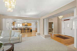 Living room with suspended lighting, light carpet, and light wood-style flooring