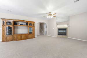 Unfurnished living room with light carpet, a ceiling fan, a glass covered fireplace, and arched walkways