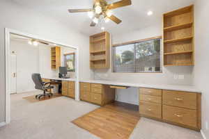 Office area featuring built in study area, ceiling fan, light carpet, and light wood finished floors