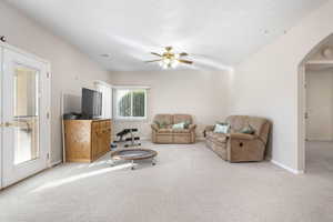 Living area featuring arched walkways, light colored carpet, and a ceiling fan