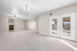 Unfurnished living room with light carpet, a glass covered fireplace, a ceiling fan, and french doors